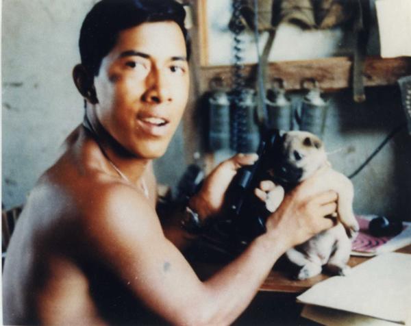 Photo of Lance Cpl. Miguel Keith deployed in Vietnam. Marine is posing with a pug and radio.