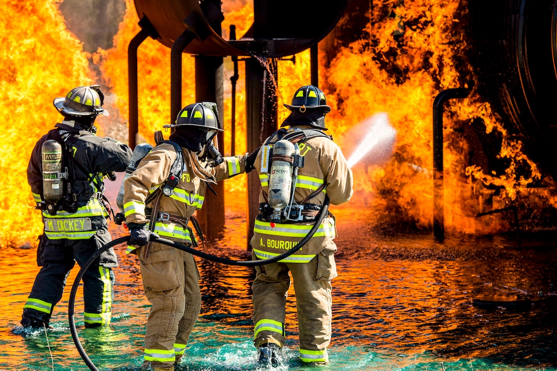Three firefighters train a hose on an engulfed simulated aircraft.