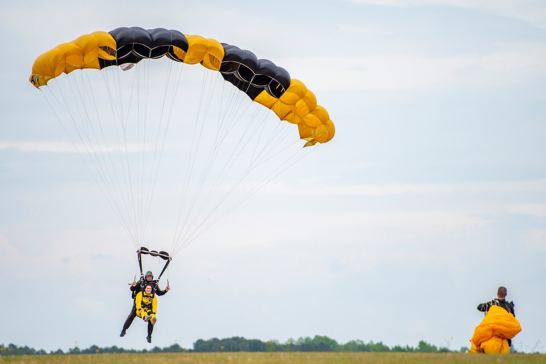Two people wearing a parachute descend in the sky.