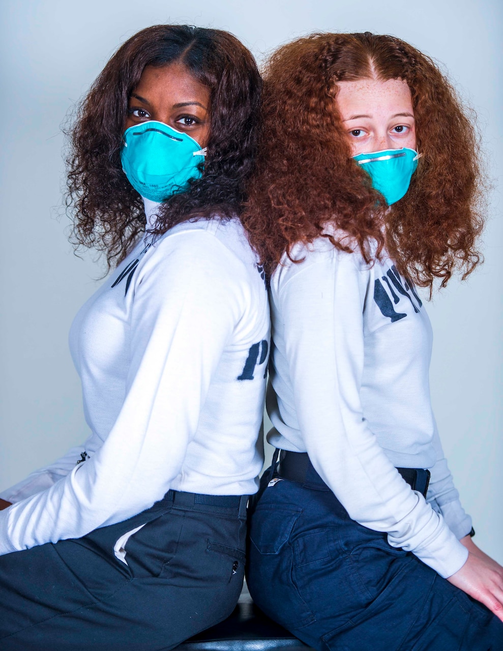Photo of two Sailors posing back to back with medical masks on with curly hair.