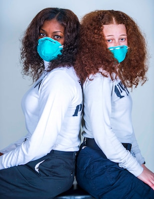 Photo of two Sailors posing back to back with medical masks on with curly hair.