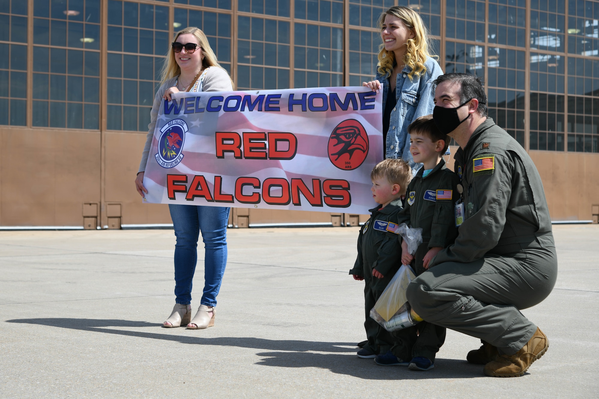 Families of deployers hold a welcome home sign April 13, 2021, at McConnell Air Force Base, Kansas. Members of the 350th Air Refueling Squadron were welcomed home by the open arms of family, friends and colleagues after a 4-month deployment to Al Udeid Air Base, Qatar. (U.S. Air Force photo by Senior Airman Nilsa Garcia)