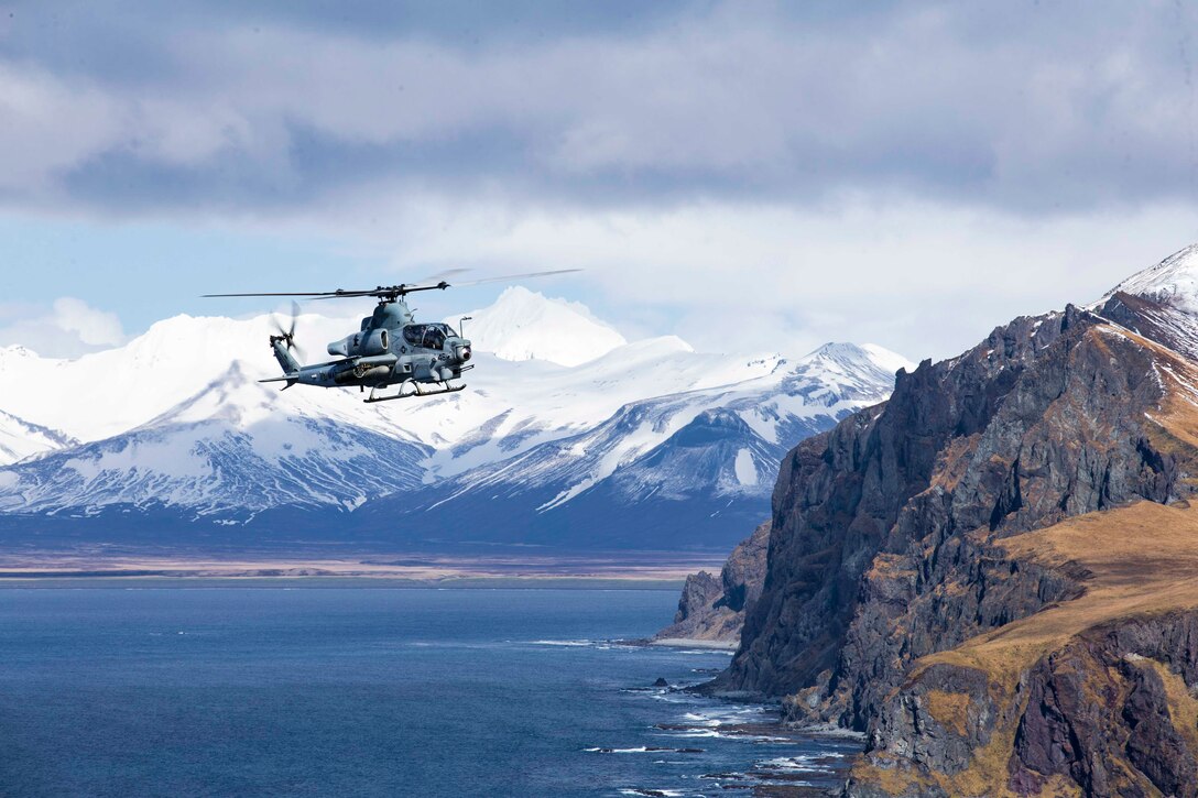 A Marine Corps helicopter flies over water near mountains.