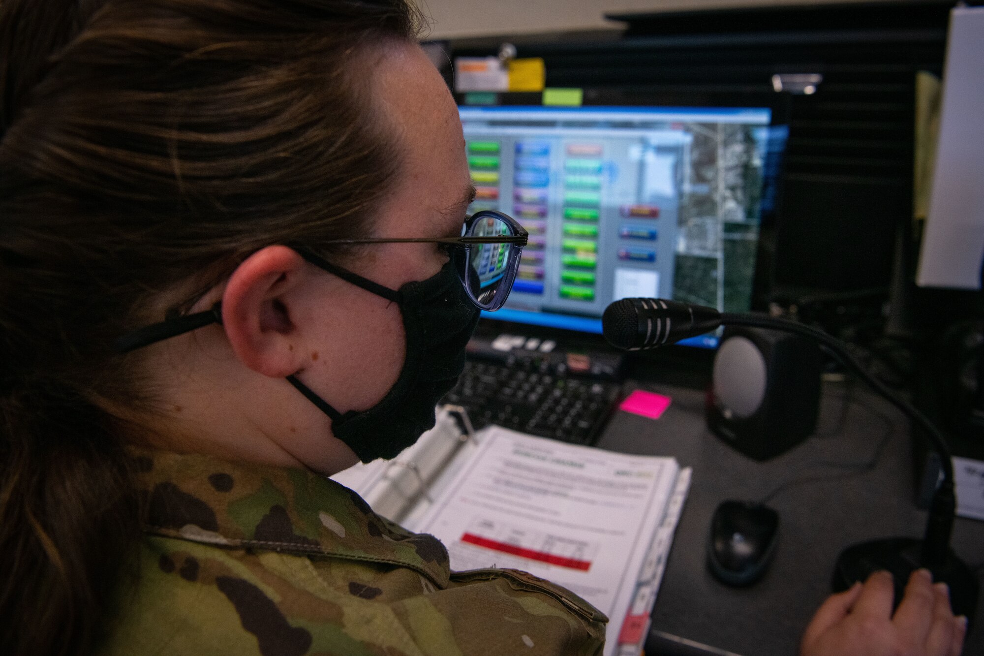 Female Airman speaks into microphone on desk with screens in background.