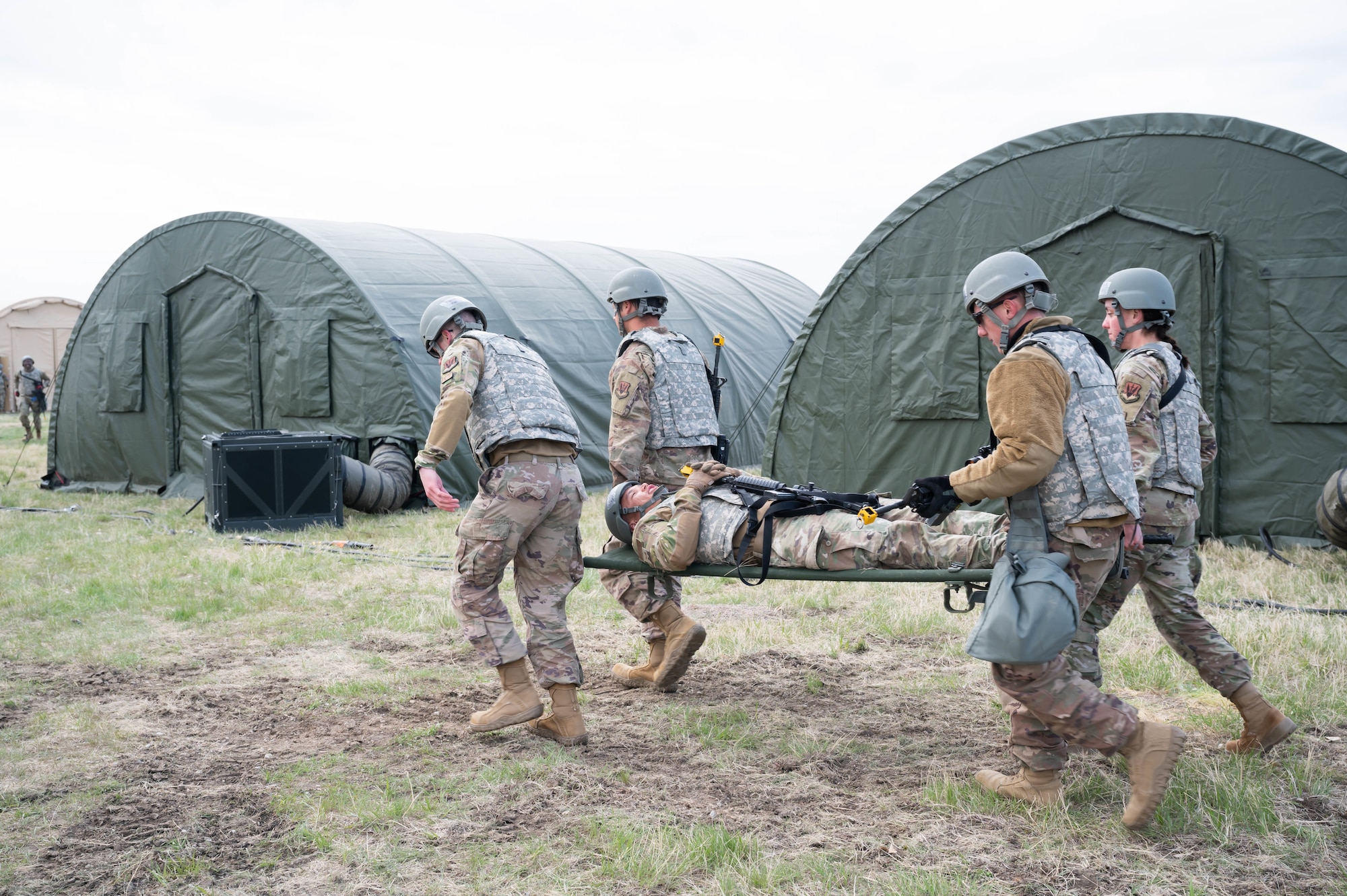 Members of the 819th RED HORSE Squadron carry an Airman on a stretcher to a simulated casualty collection point during an exercise May 4, 2021, at Malmstrom Air Force Base, Mont.