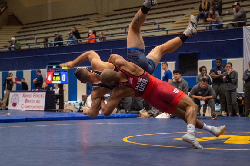 Two wrestlers wrestle in a gym.