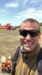 Man taking selfie in front of helicopter with inset of family on screen.