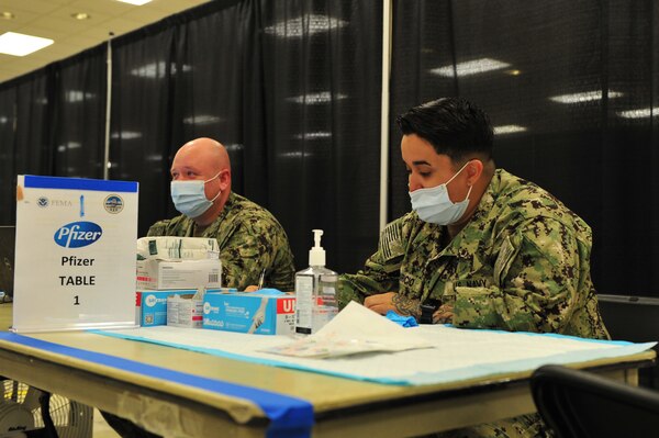 Hospital Corpsman 3rd Class Blake Faletti and Hospitalman Shelby Aparicio prepare their station as they await patients arrival to administer the Pfizer vaccine at the state-run, federally-supported COVID-19 Community Vaccination at Norfolk.