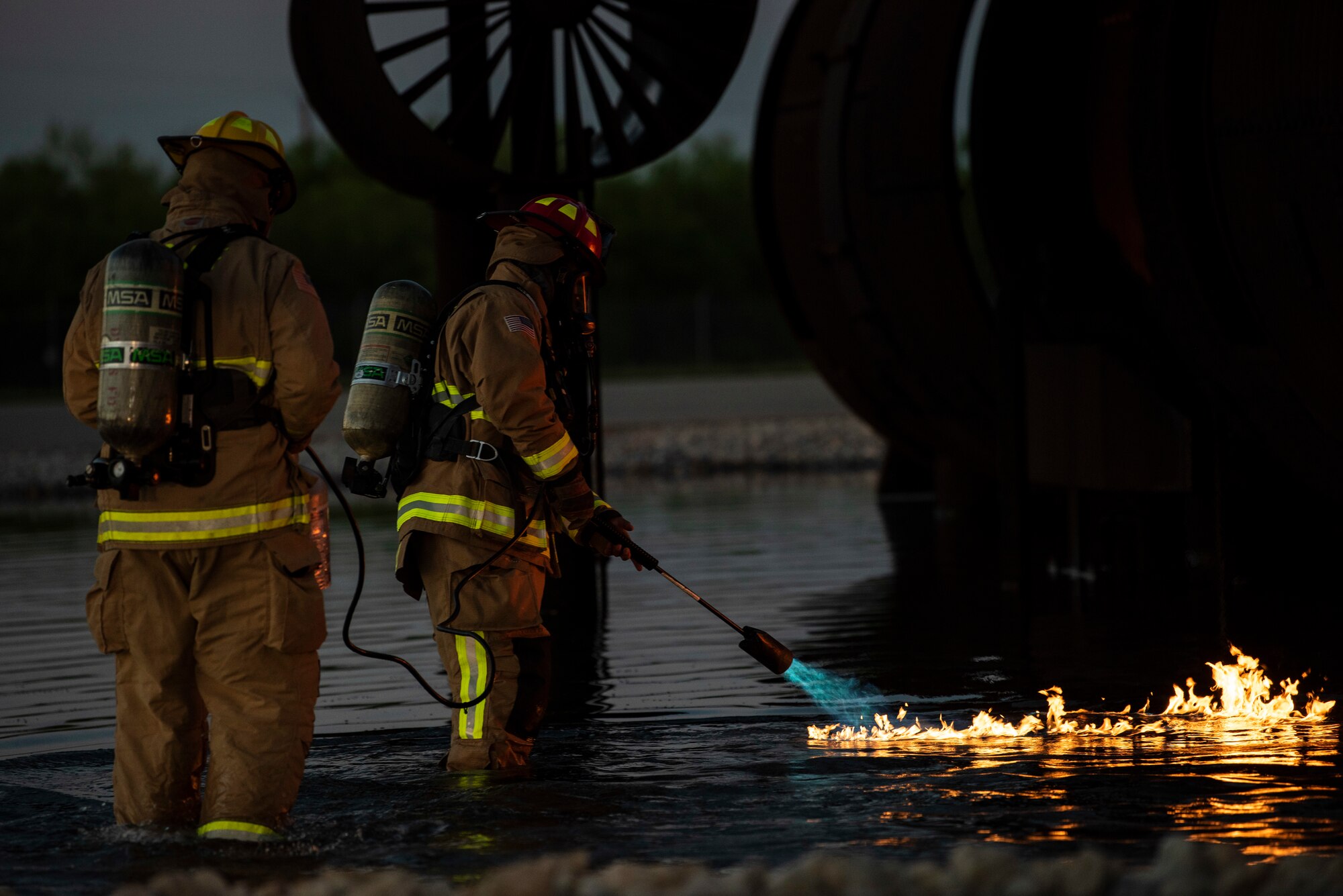 Two firefighters assigned to the 7th Civil Engineer Squadron ignite a fire during a nighttime aircraft fire training at Dyess Air Force Base, Texas, May 4, 2021. During the live fire training, a flammable gas was ignited on the surface of the water to simulate the pooling and burning of jet fuel around an aircraft. (U.S. Air Force photo by Airman 1st Class Colin Hollowell)