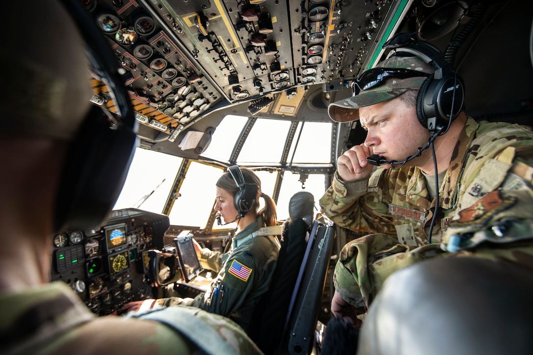 An airman monitors gauges while sitting in a cockpit with fellow airmen.