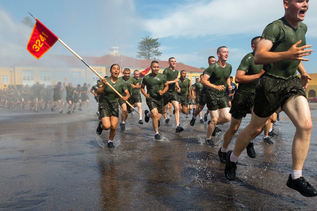 A Marine carries a flag while running through water with fellow Marines.