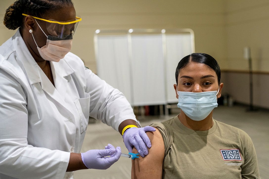 An Army ROTC cadet sits as a medical professional gives her a shot in her right arm.
