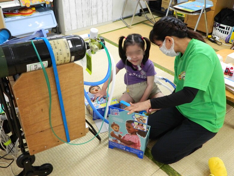 第３海兵遠征旅団の海兵隊員らが自前で購入した沢山のおもちゃを貰い笑顔を見せる医療型児童デイサービスの女の子
