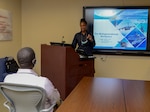 A woman stands behind a podium looking at a seated man who is one of her students in a training class.