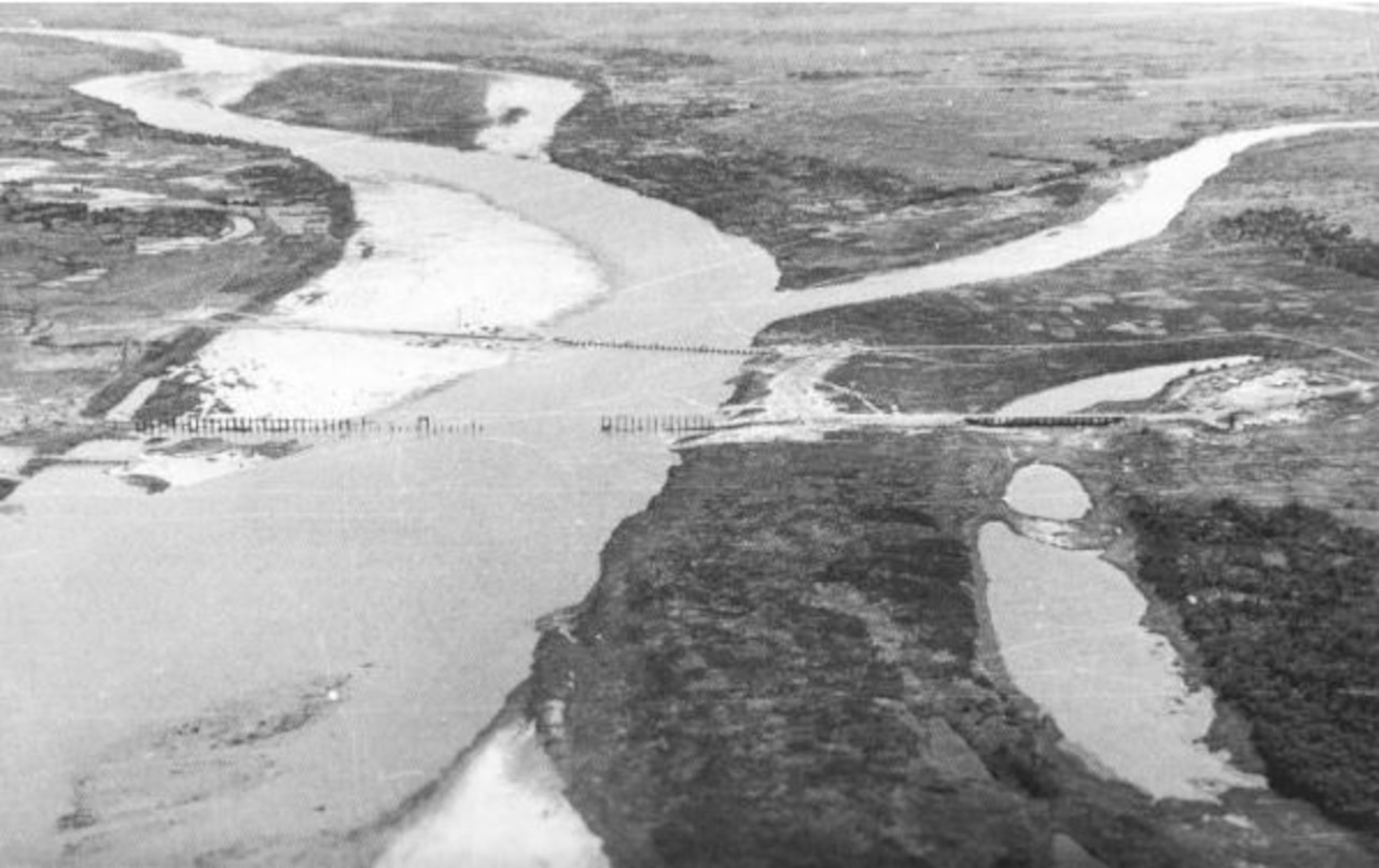 An aerial photo shows a waterway and land connected by two bridges, one of which has partially collapsed.