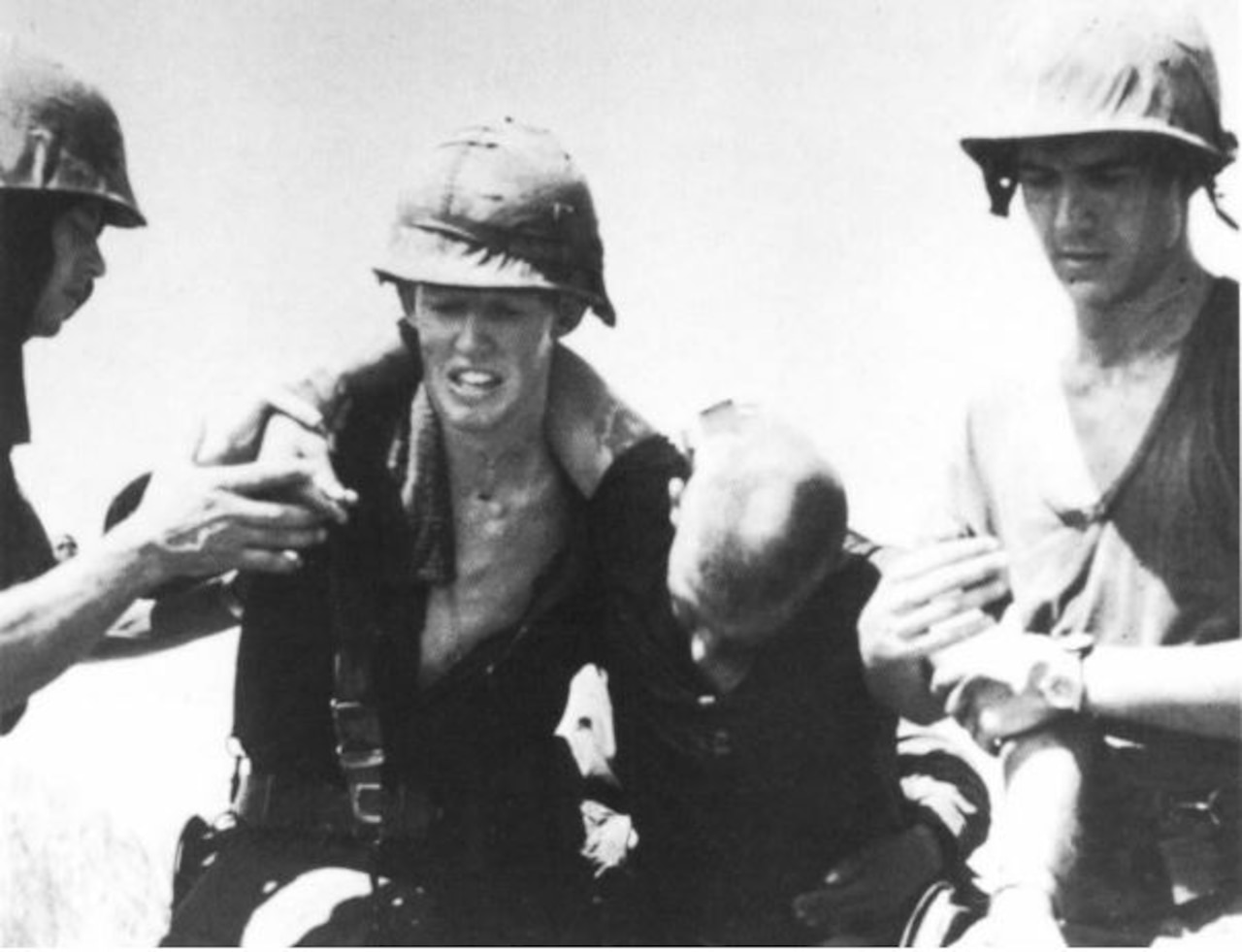 Two men in combat helmets carry another man.