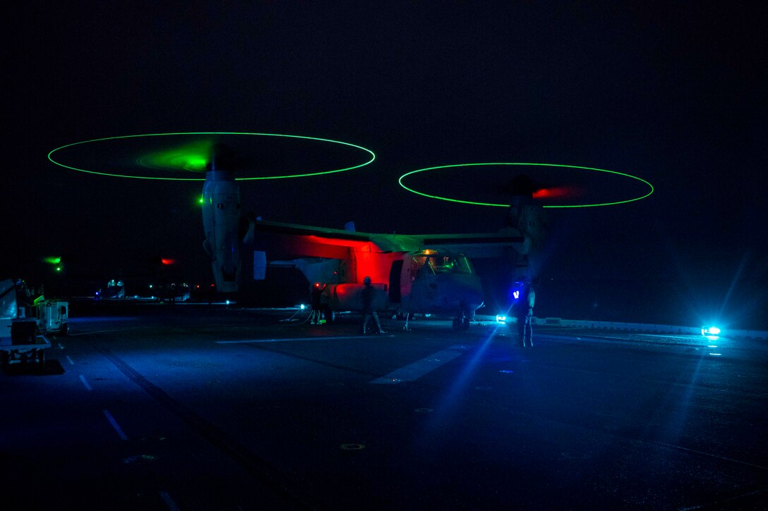 A Marine Corps aircraft sits parked on the deck of a ship at night.