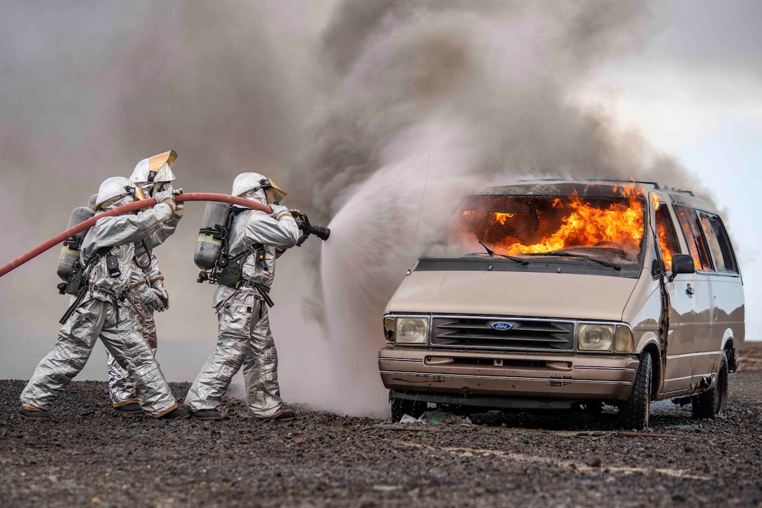 Two Marines use a hose to spray water onto a vehicle fire.