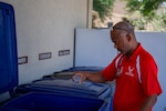 Man putting plastic bottle in blue recycling bin.