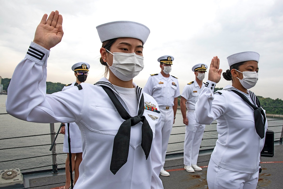 Two sailors stand with right hands raised aboard a ship's deck.
