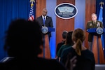 Two men at lecterns as reporters ask questions.