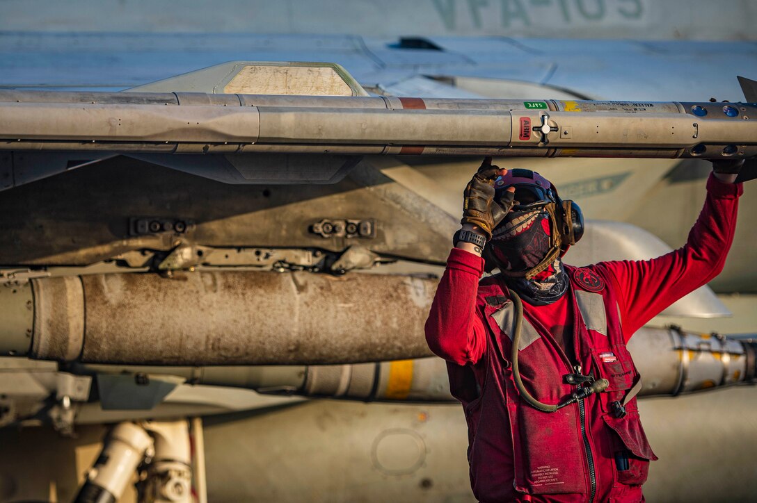 A sailor checks ordnance on an aircraft.