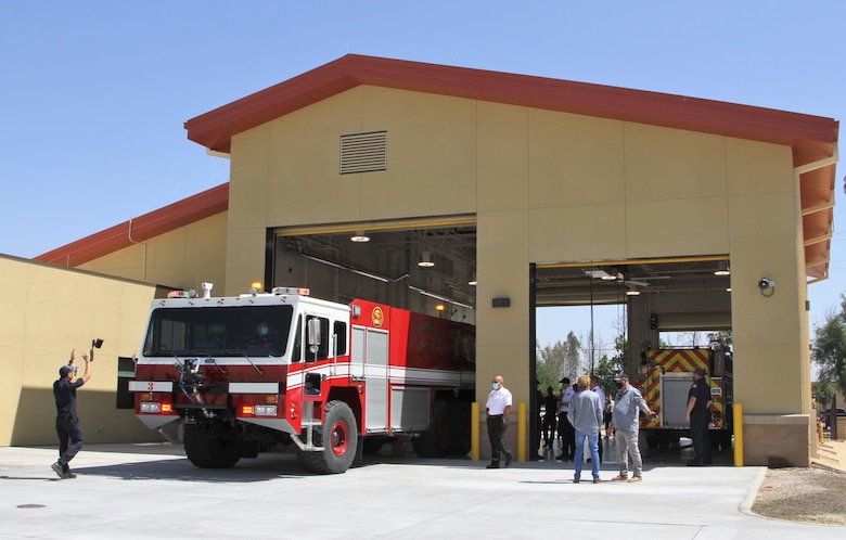 Leaders, firefighters, project engineers and contractors explore the newly constructed fire station at March Air Reserve Base in Riverside County, California, after its official unveiling May 6, 2021, while a firefighter directs a flight-line crash truck into one of the facility’s two drive-through bays. The project was managed by the U.S. Army Corps of Engineers Los Angeles District.