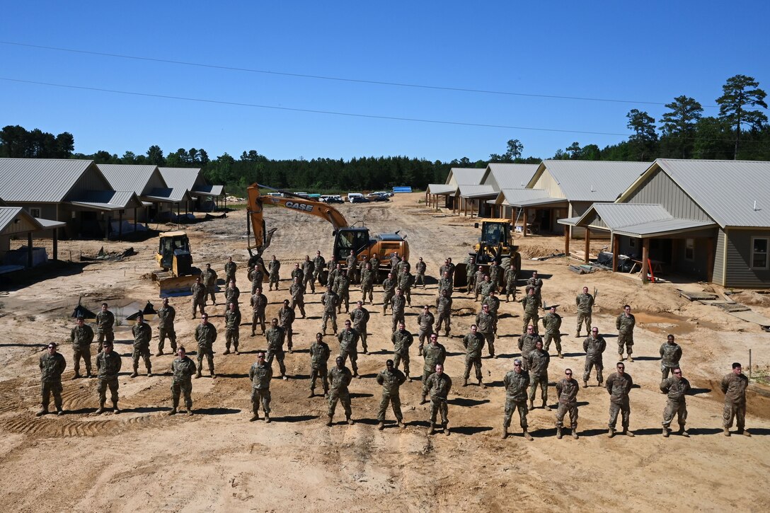 Photo of Airmen posing in formation with construction equipment in the background.
