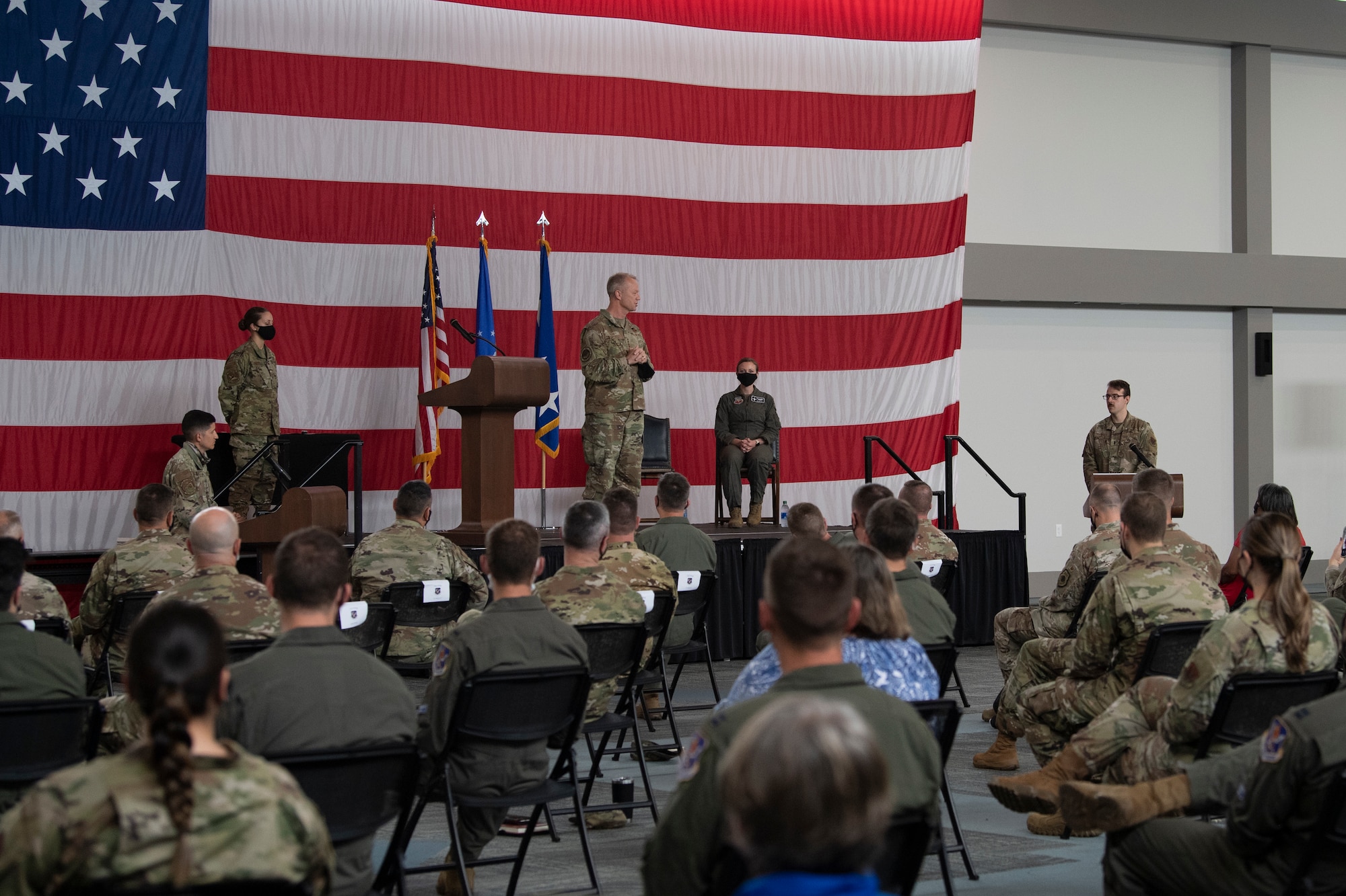 A photo of Gen. Kelly on a stage, with an American flag in the background, in front of a crowd.