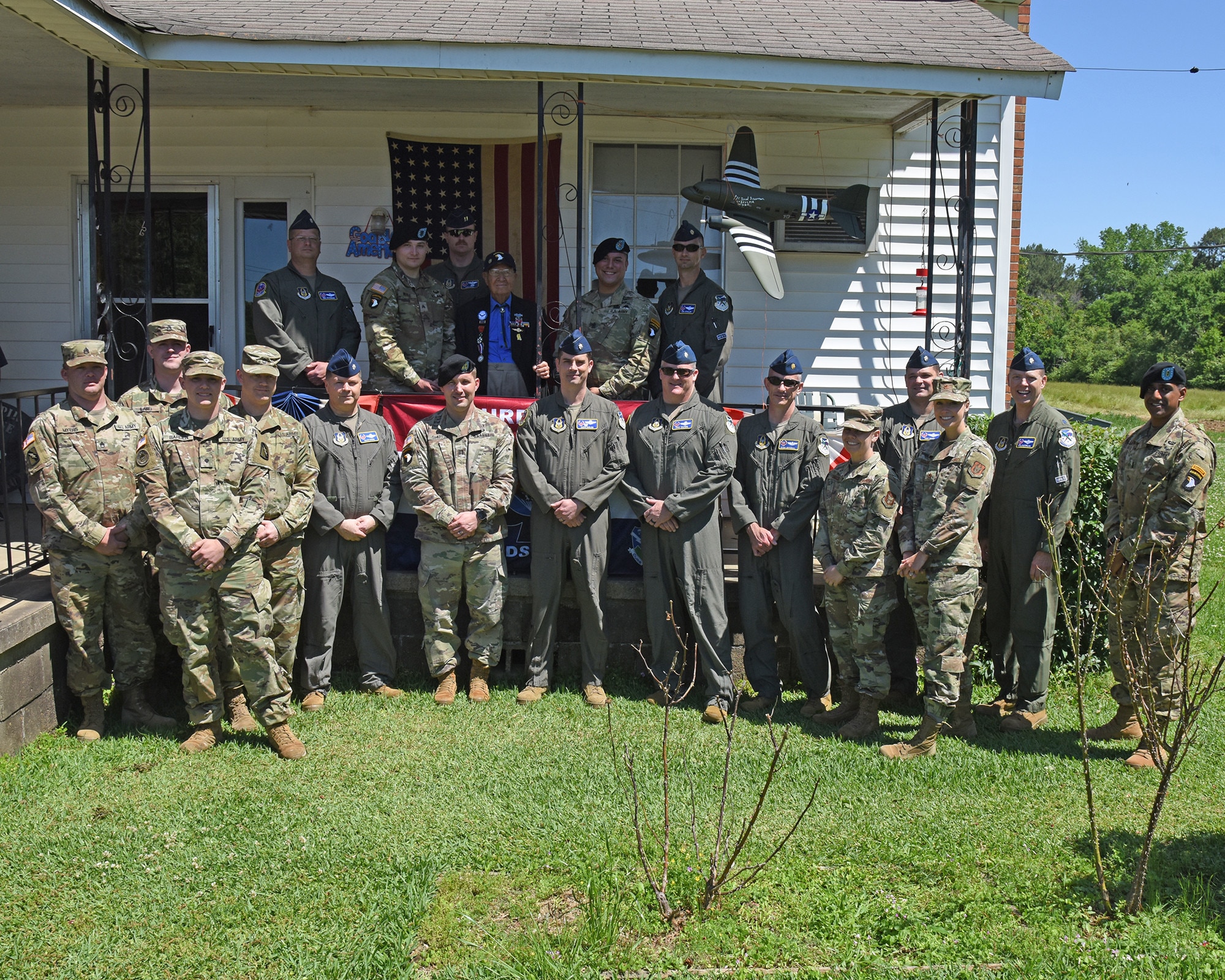 Military members pose with a WWII veteran outside his home.