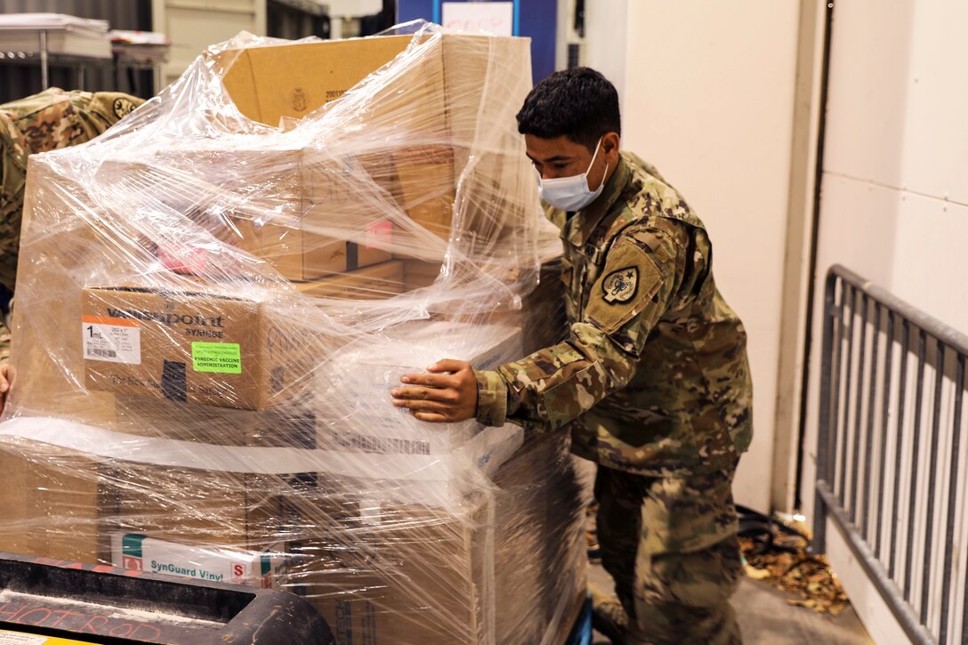 A soldier wearing a face moves a pallet containing medical supplies.