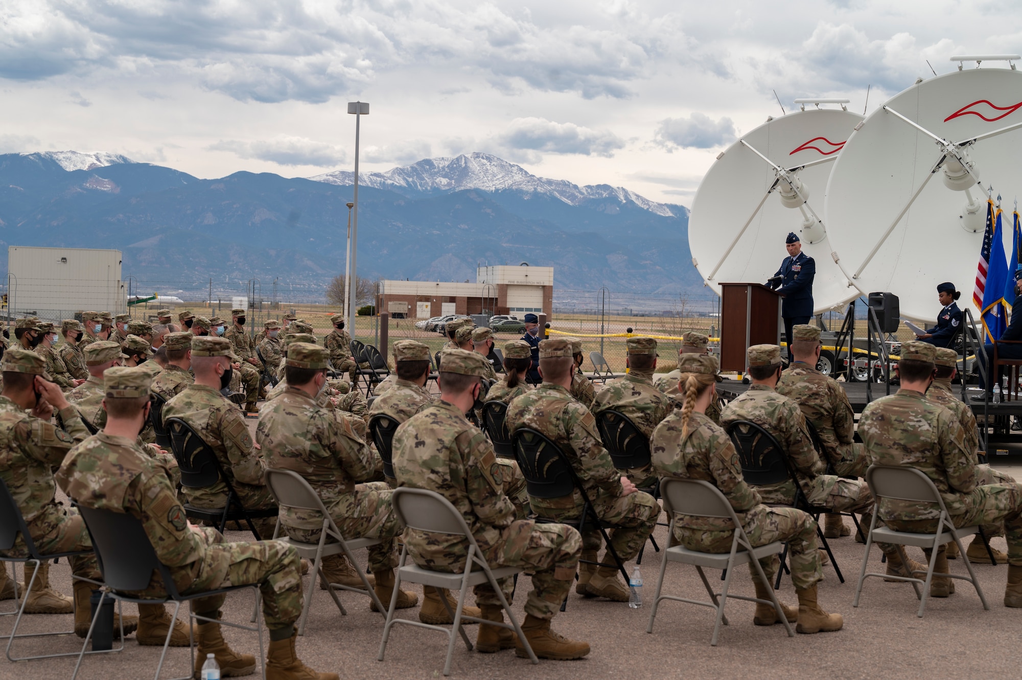 A man speaks in front of a sitting crowd outside.