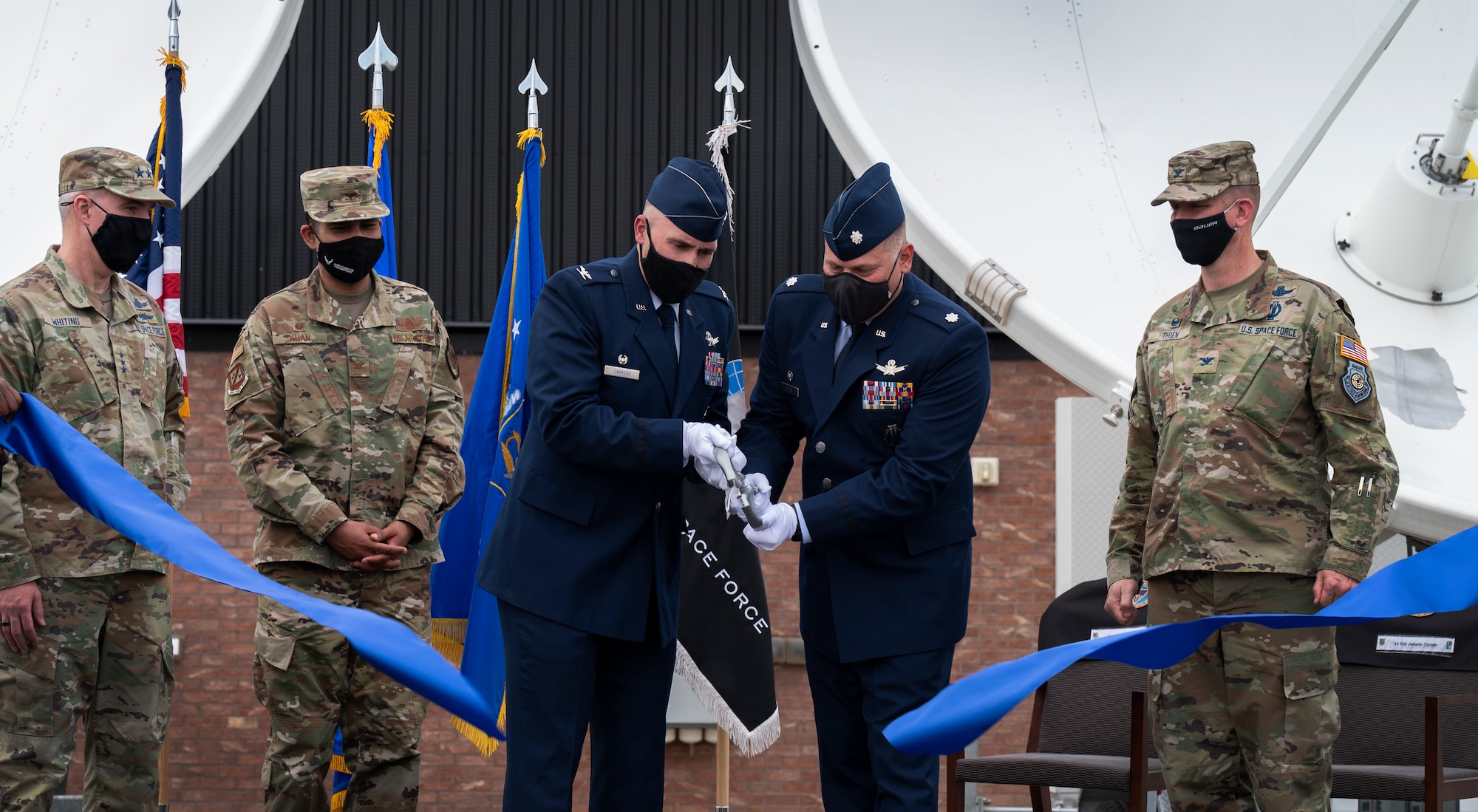 Two men cut a ceremonial ribbon on stage with oversized scissors.