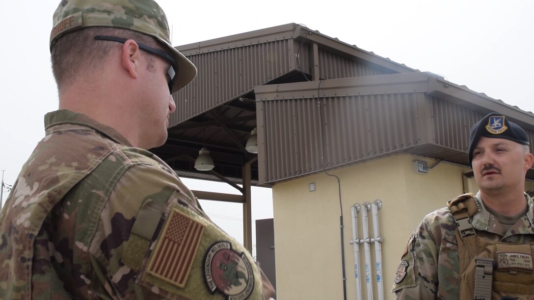 One explosives ordnance disposal Airman and a security forces Airman stand next to each other talking