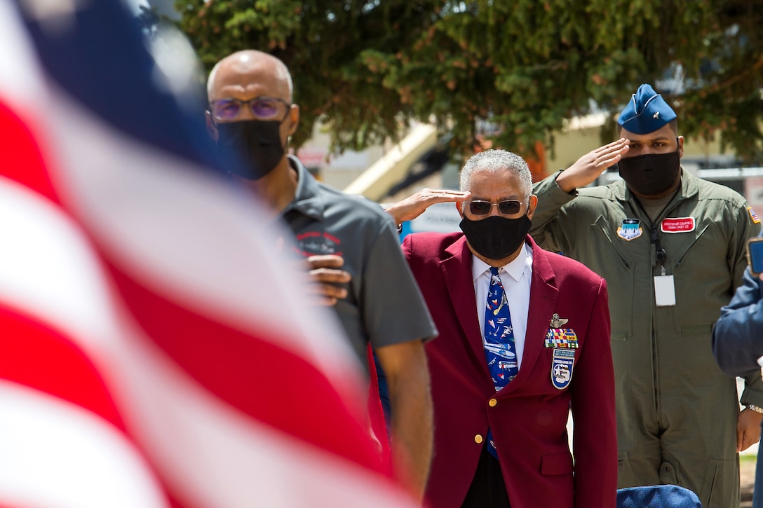 A group of people salute as an American flag flutters in the foreground.