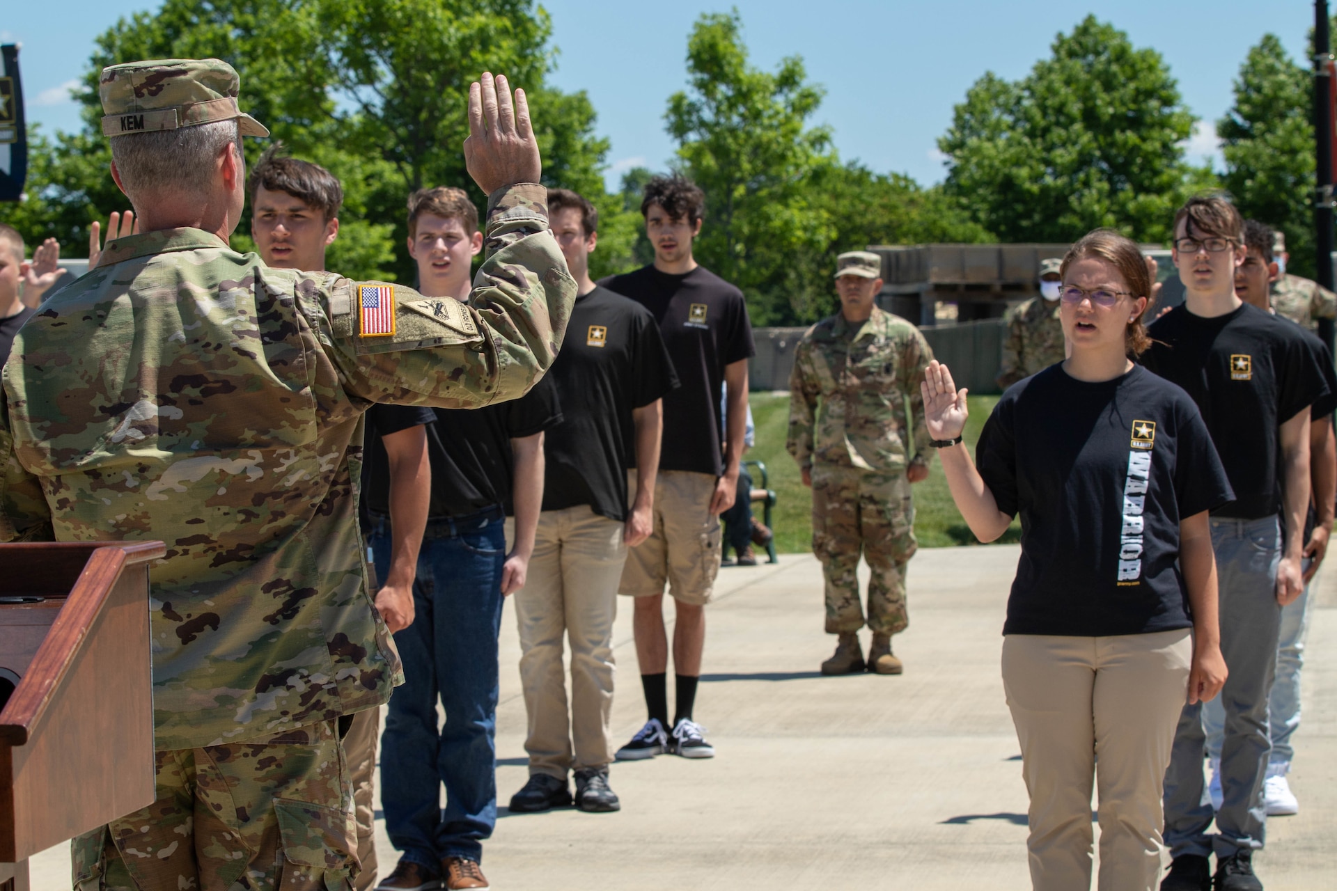 man in uniform with his right hand raised, in front of multiple young people holding up their right hand.