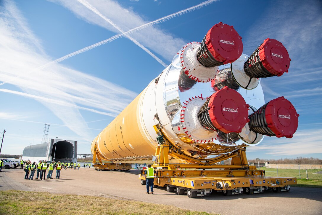 A large rocket, several meters tall, is transported on its side to a large hanger facility.