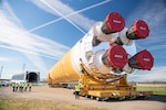 A large rocket, several meters tall, is transported on its side to a large hanger facility.