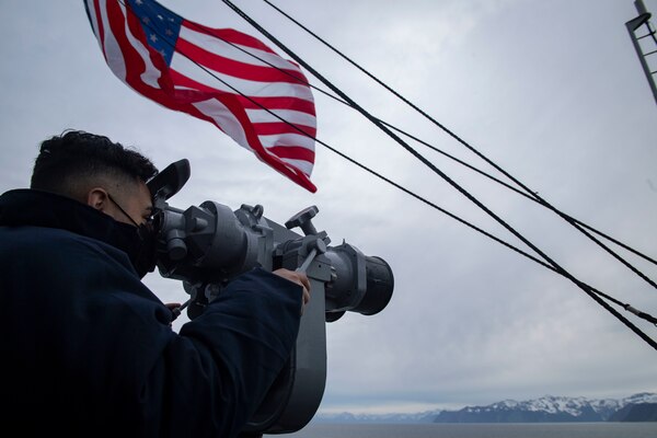 A Sailor looks through ship-mounted binoculars from the aircraft carrier USS Theodore Roosevelt (CVN 71), May 7, 2021, in support of flight operations