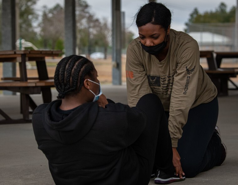A trainee holds the feet of another trainee down while she does sit-ups.
