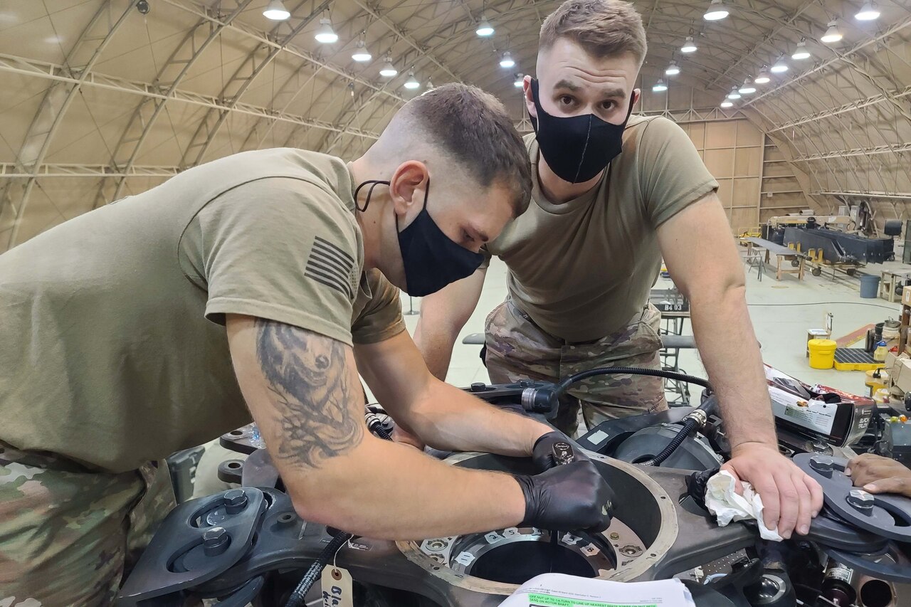 Two men work on a helicopter inside a hangar.