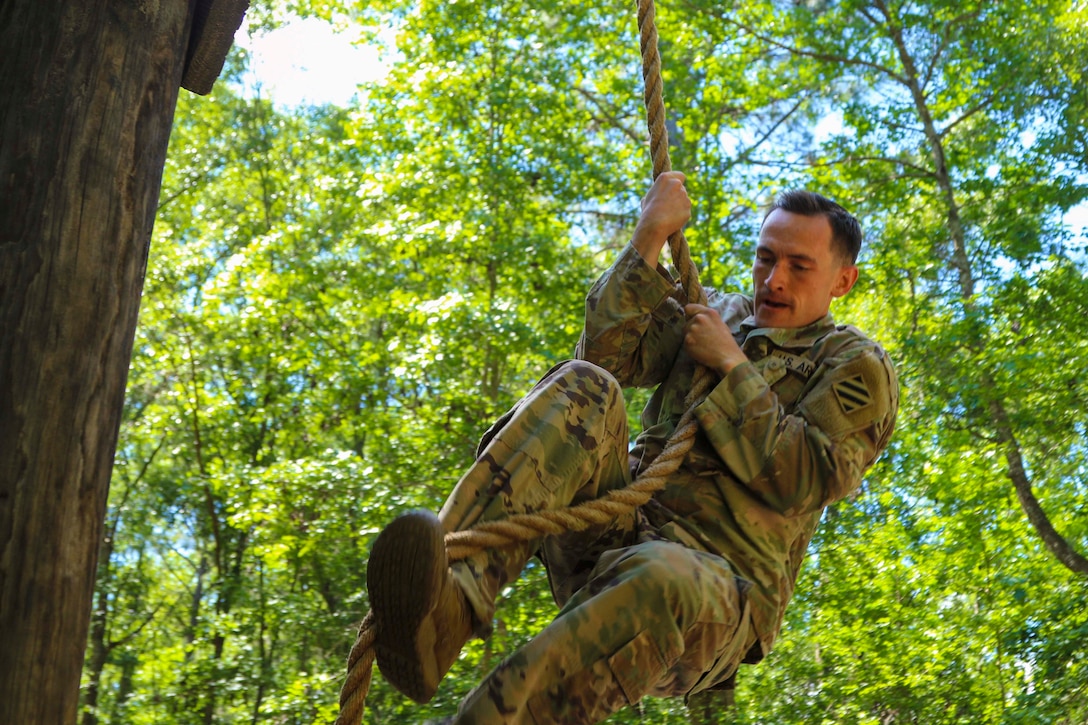 A soldier climbs a rope in a wooded area.