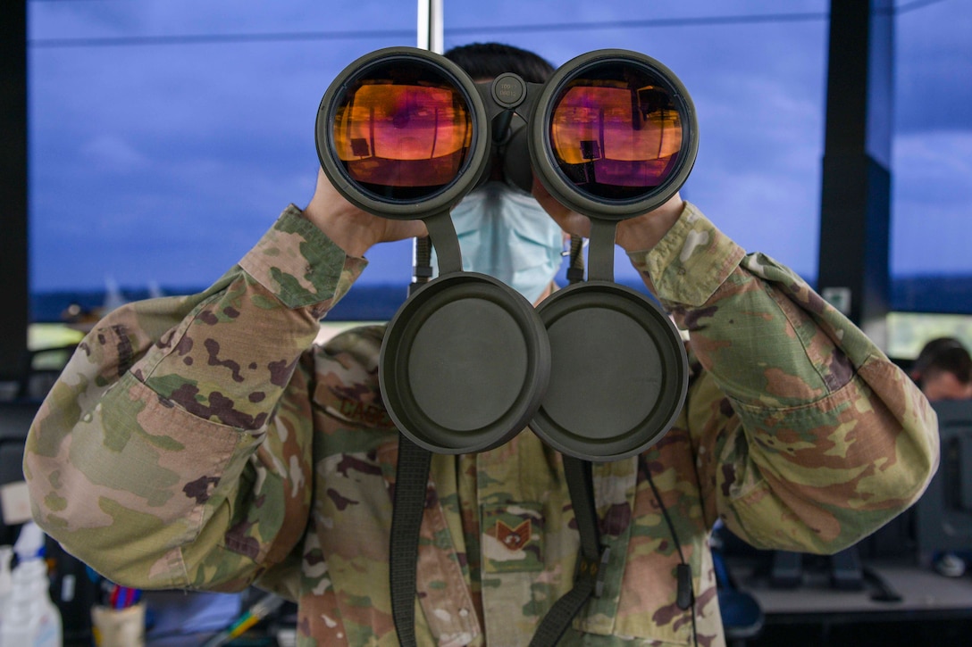 An airman looks through a large pair of binoculars.