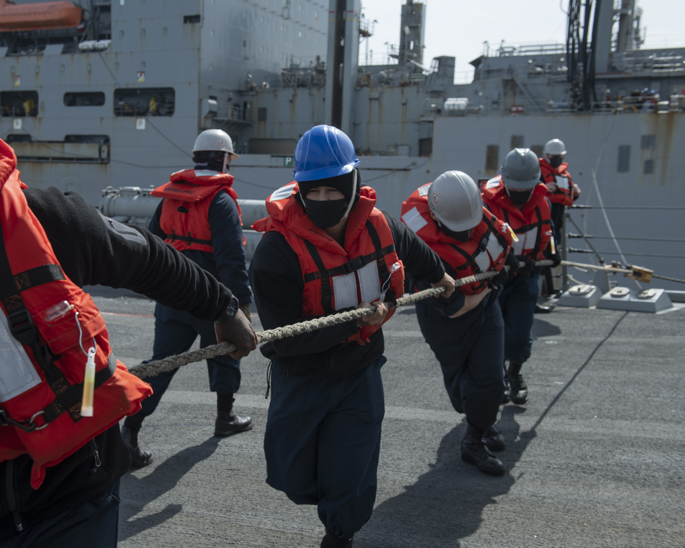 Sailors aboard destroyer USS Rafael Peralta (DDG 115) haul in the spanning wire from the USNS Amelia Earhart (T-AKE-6) during a vertical replenishment (VERTREP).