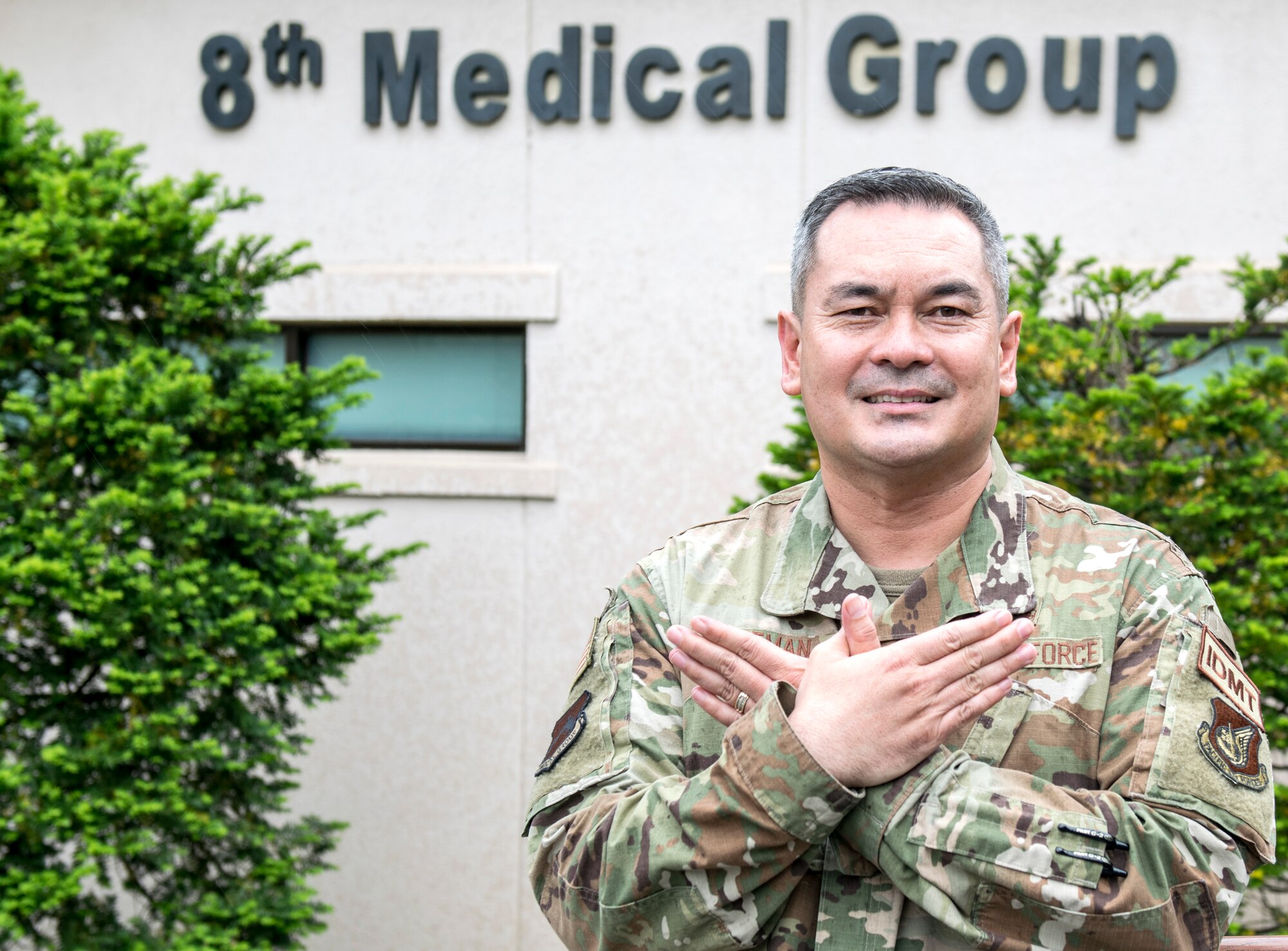Chief master sergeant Joe Dittman folds his hands like a bird, which is the hawk hand sign, in front of the 8th Medical Group building