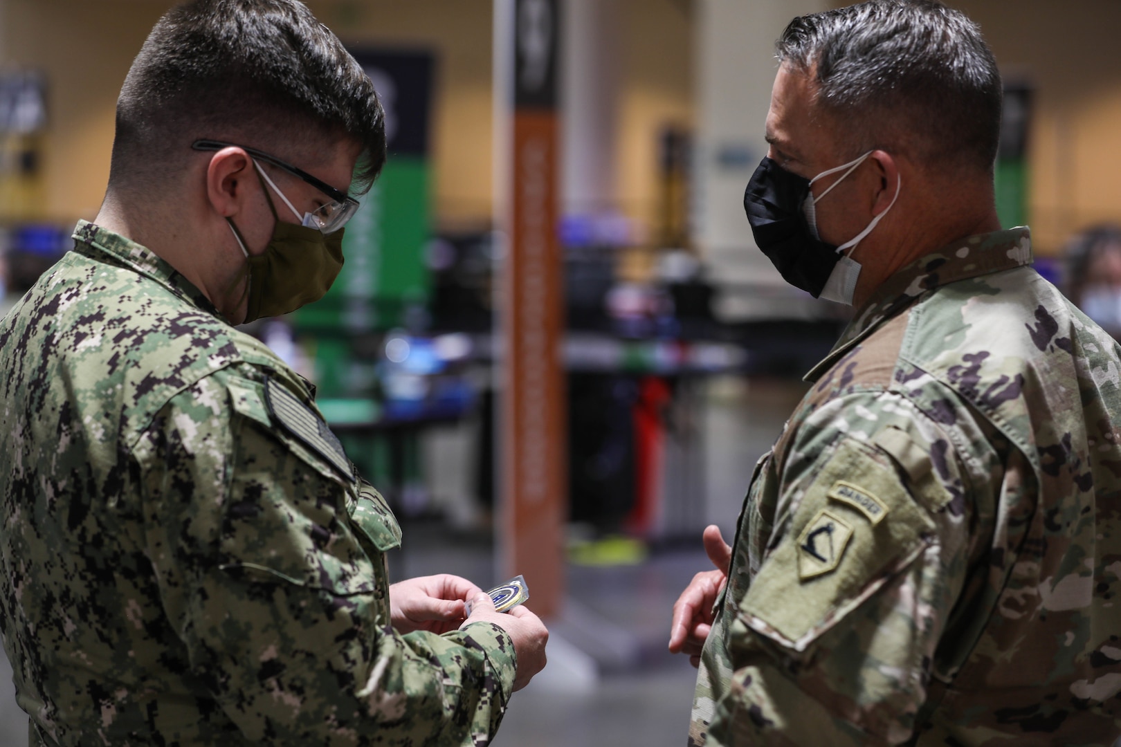 U.S. Navy Petty Officer 3rd Class Bake Sylvester, left, assigned to Naval Medical Center Portsmouth, Virginia, receives a coin from U.S. Army Brig. Gen. Ronald Cupples, right, the assistant adjutant general for the Massachusetts National Guard, at the Community Vaccination Center at the Hynes Convention Center in Boston, April 30, 2021.