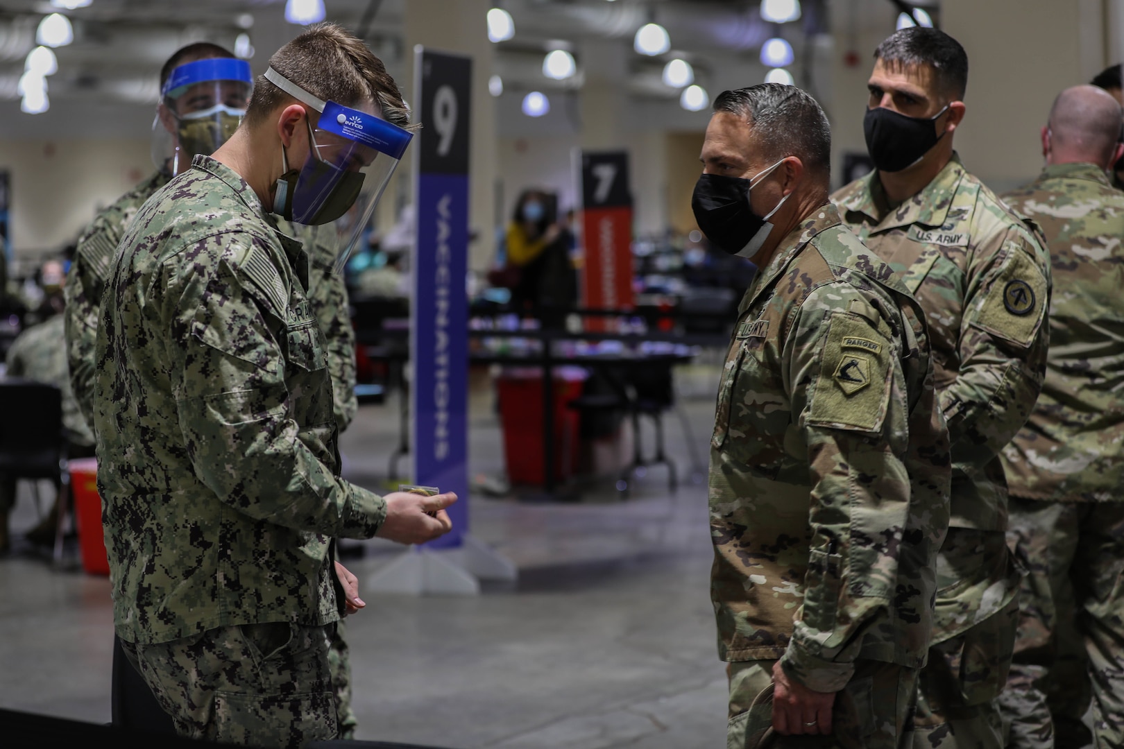 U.S. Navy Hospitalman  Dylan Crawford, left, assigned to Naval Medical Center Portsmouth, Virginia, receives a coin from U.S. Army Brig. Gen. Ronald Cupples, right, the assistant adjutant general for the Massachusetts National Guard, for being the Vaccinator of the Week, April 19-25, and vaccinating approximately 840 local community members, at the Community Vaccination Center at the Hynes Convention Center in Boston, April 30, 2021.