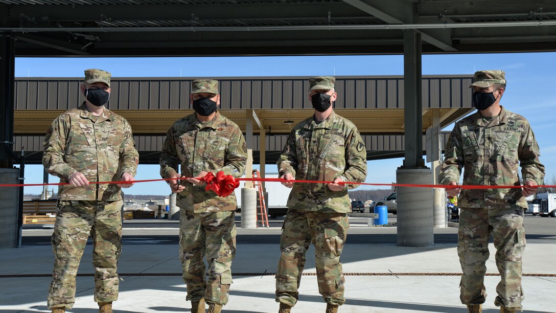 four military men stand to cut a ribbon