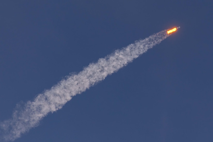 A rocket arcs across a blue sky.