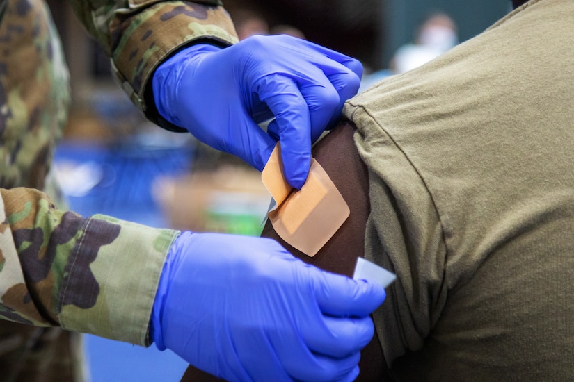 A soldier wearing gloves gives another soldier a  vaccine.